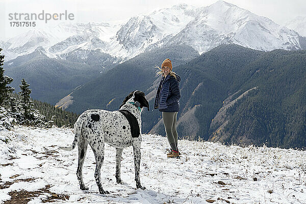 Frau wandert im Urlaub mit Hund auf schneebedecktem Berg