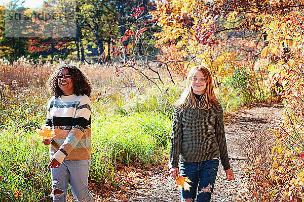 Zwei hübsche Tween-Mädchen lachen gemeinsam draußen in Herbstfarben.