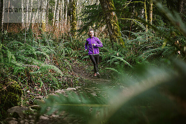 Läuferin in lila Jacke auf felsigem Weg  umgeben von Farnen
