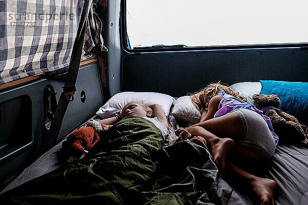 Zwei Mädchen schlafen im Van beim Zelten im Morgengrauen