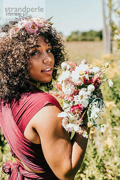 Schwarze Frau hält einen Strauß rosa Blumen vor ihr Gesicht