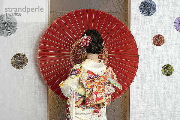 Weiblicher Erwachsener im Kimono mit ausgebreitetem Regenschirm
