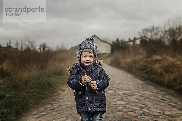 Porträt eines kleinen Jungen  der auf der Straße steht und einen kleinen Zweig in der Hand hält