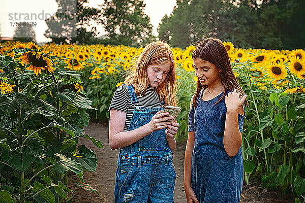 Zwei glückliche Teenager-Mädchen in einem Sonnenblumenfeld.