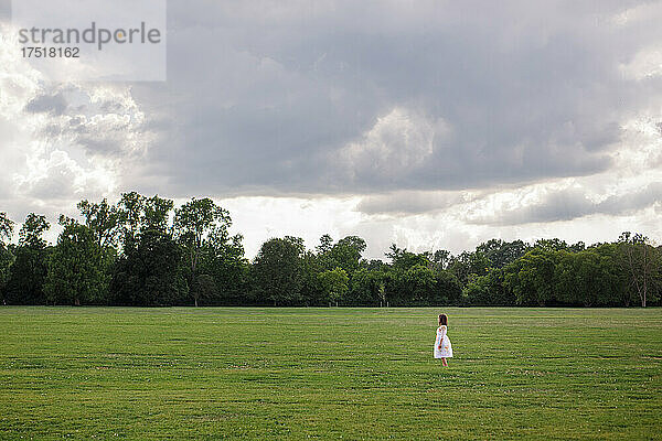 Ein kleines Kind steht allein auf einem großen Feld unter stürmischem Himmel