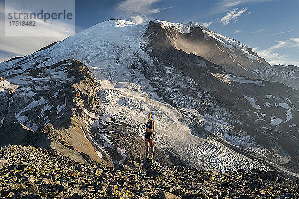 Fitte Frau steht auf einer Klippe neben dem Mount Rainier und lächelt in die Kamera