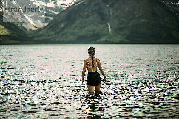 Junges Teenager-Mädchen blickt auf Berge  während es im See steht