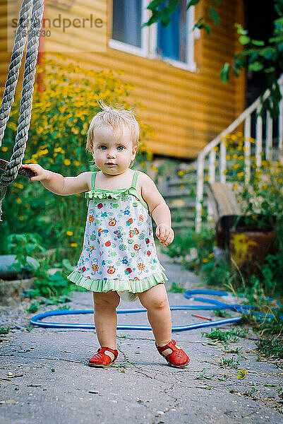 Süßes 3-4-jähriges Mädchen spielt im Garten eine rustikale Schaukel