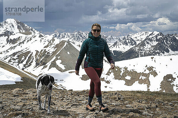 Glückliche Wanderin wandert mit Hund auf dem Berg vor bewölktem Himmel
