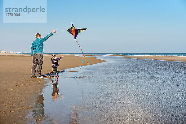 Vater und Kind lassen an einem sonnigen Wintertag am Strand Drachen steigen