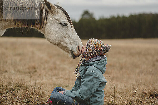 Teenager-Mädchen sitzt vor Pferd und küsst die Nase