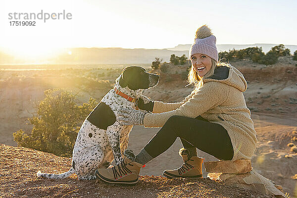 Porträt einer glücklichen Frau mit Hund  die in der Wüste sitzt