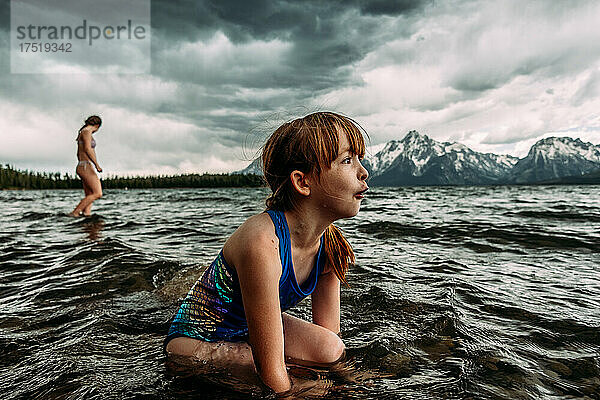 Verblüfftes junges Mädchen blickt auf Berge  während es im See sitzt
