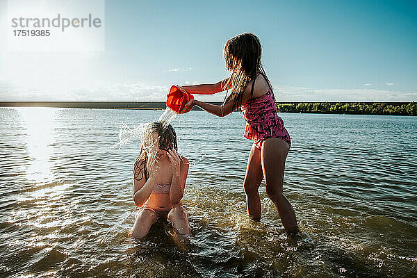 Junges Mädchen schüttet Wasser auf den Kopf ihrer Schwester
