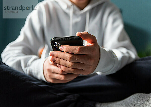 Nahaufnahme der Hände eines Teenagers im weißen Pullover  der am Telefon SMS schreibt.