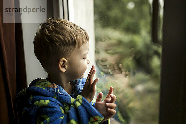 Seitenansicht eines Jungen  der sein Spiegelbild im Fenster betrachtet