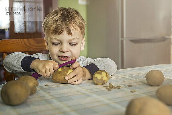 Kleiner blonder Junge lernt  wie man Kartoffeln mit dem Schäler Sitti schält