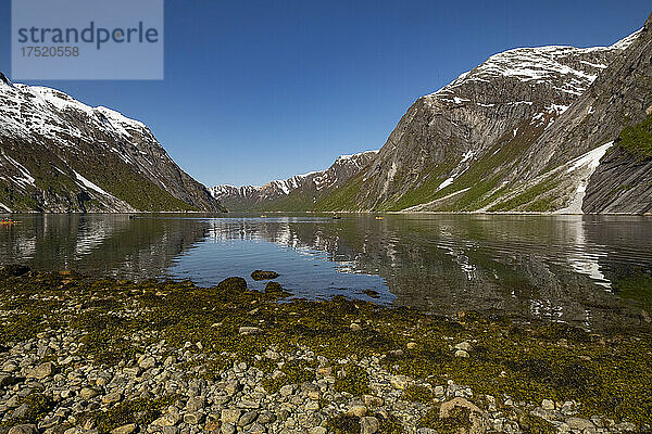 Schneebedeckte Berge spiegeln sich im stillen Wasser des Fjords  wo Kajakfahrer die Aussicht genießen  Nordfjord  Norwegen  Skandinavien  Europa