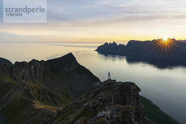 Tourist betrachtet den Fjord im Morgengrauen und steht auf dem Gipfel des Berges Husfjellet  Insel Senja  Kreis Troms  Norwegen  Skandinavien  Europa