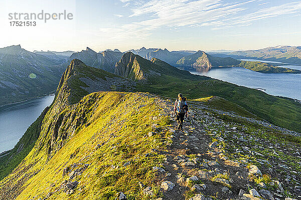 Rückansicht eines Mannes  der bei Sonnenaufgang auf dem Weg zum Berggipfel Husfjellet geht  Insel Senja  Kreis Troms  Norwegen  Skandinavien  Europa