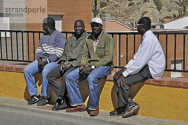 Afrikanische Männer sitzen auf Mauer eines Gartenzaun  Cuevas del Almanzora  Andalusien  Spanien  Europa