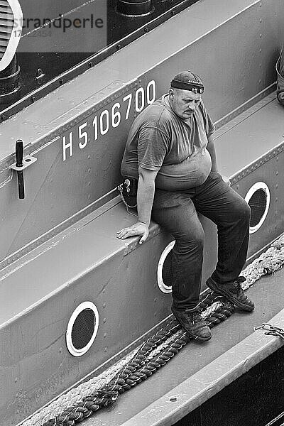 Dickbauchiger Seemann mit Mütze sitzt nachdenklich auf Schiff  Hamburg  Deutschland  Europa