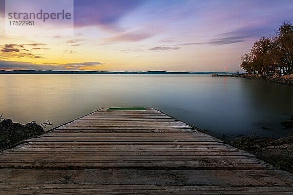 Ufer an einem See  ein Steg geht in den See. Im Hintergrund ist eine Bootanlegestelle mit Sonnenuntergang  langzeitbelichtung Siofok  Balaton  Plattensee  Ungarn  Europa