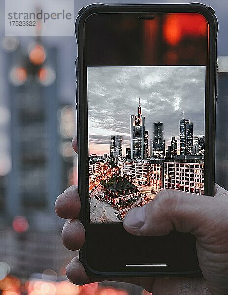 Die Hauptwache  Blick von oben auf einen Platz mit Geschäften und Restaurants  im Hintergrund die Skyline Beleuchtet am Abend  Hand hält Handy  Handyfoto  Frankfurt  Hessen  Deutschland  Europa
