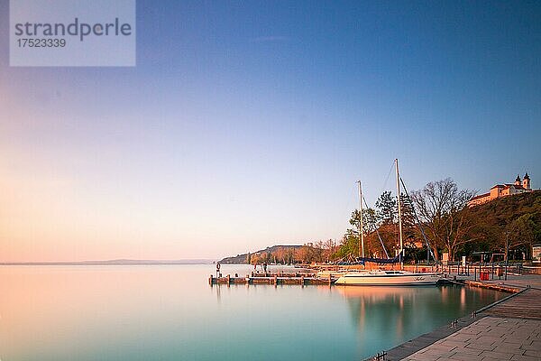 Ufer an einem See  mit Booten. Im Hintergrund ist die Abtei  Kirche von Tihany und es geht die sonne auf  Balaton  Plattensee  Ungarn  Europa