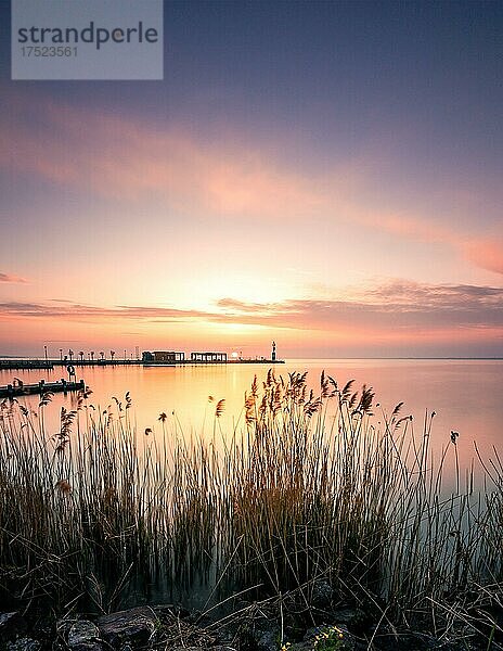 Ufer an einem See  mit schilf. Im Hintergrund ist eine Bootanlegestelle und es geht die sonne auf  tihany  Balaton  Plattensee  Ungarn  Europa