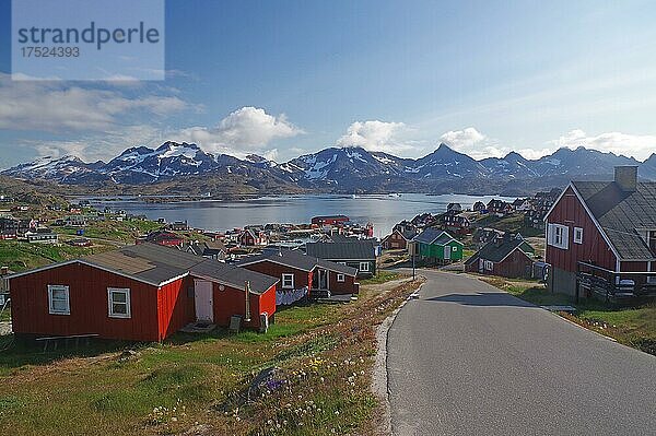 Rote Holzhäuser verteilen sich weitläufig  karge Berge mit Schnee und ein Fjord  Tasilaq  Arktis  Ostgrönland  Grönland  Dänemark  Nordamerika