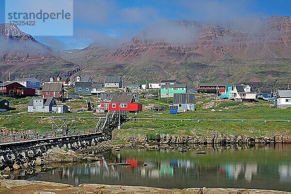 Einfache Brücke führt zu Häusern  die sich in einem Gewässer spiegeln  auflösender Nebel und rotes Vulkangestein  Nebelwand  rotes Vulkangestein  Diskoinsel  Diskobucht  Qeqertarsuaq  Arktis  Grönland  Arktis  Dänemark  Nordamerika
