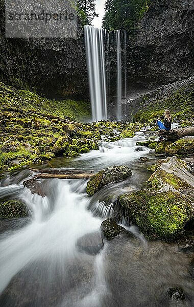 Junge Frau sitzt auf am Fluss  Wasserfall stürzt über Felsvorsprung herab  Tamanawas Falls  Langzeitaufnahme  Wildfluss Cold Spring Creek  Oregon  USA  Nordamerika