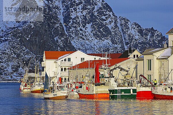 Kleine Fischerboote vor Holzhäusern im winterlichen Abendlicht  verschneite Berge  Henningsvaer  Austvågøy  Nordland  NorwegenAustvågøy