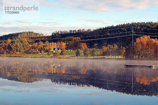 Nebelschwaden über einem See  Bäume und Häuser spiegeln sich im ruhigen Wasser eines See  Oktober  Laubfärbung  Badeinsel  Vassstoppen  Bohuslän  Bullaren  Schweden  Europa