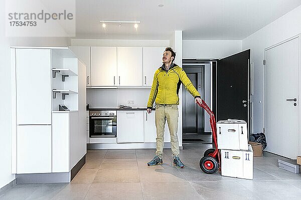Junger Mann mit Umzugskisten  steht in moderner Küche einer Wohnung  Umzug in eine Neue Wohnung  München  Bayern  Deutschland  Europa