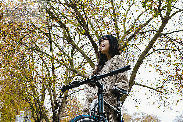 Lächelnde Frau lehnt auf Fahrrad unter Baum