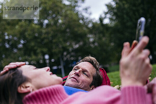 Thoughtful man lying with woman holding smartphone at park