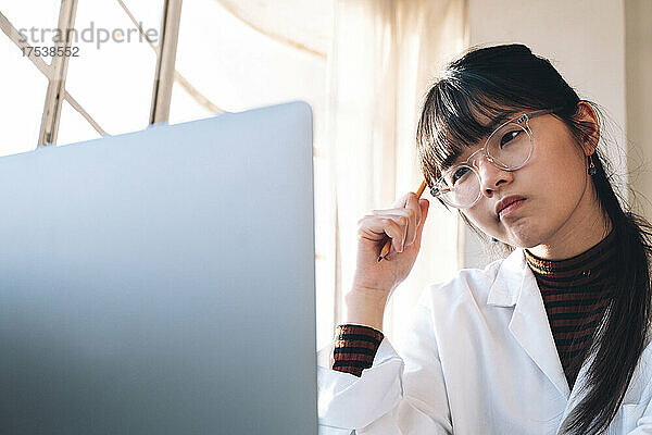 Junger Chemiker denkt nach  während er im Labor auf den Laptop schaut