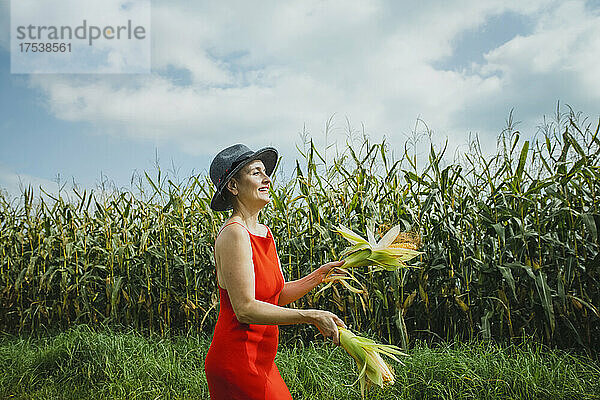 Woman wearing hat and red dress juggling corns walking at field