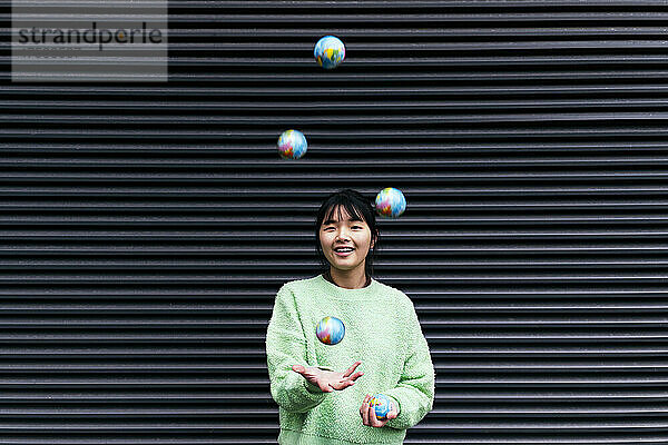 Woman juggling with globe balls in front of black corrugated wall