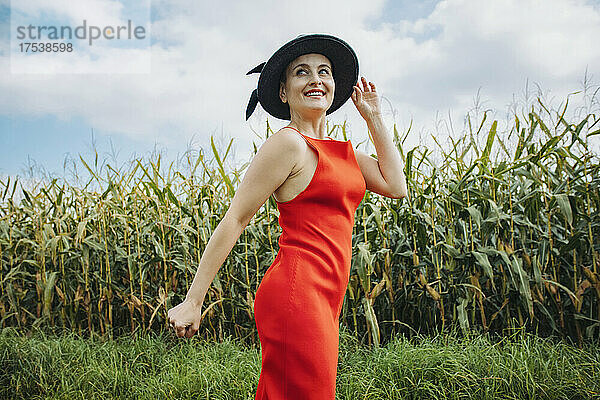 Lächelnde schöne Frau mit Hut  die vor einem Maisfeld steht