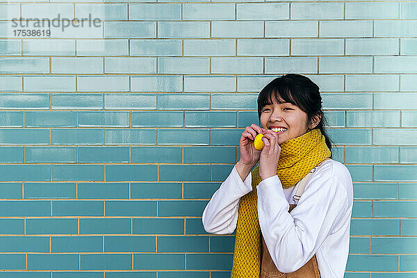 Smiling woman holding balloon in front of brick wall