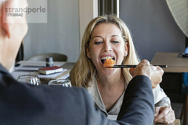 Mann füttert Frau beim Mittagessen im Restaurant mit Stäbchen mit Sushi