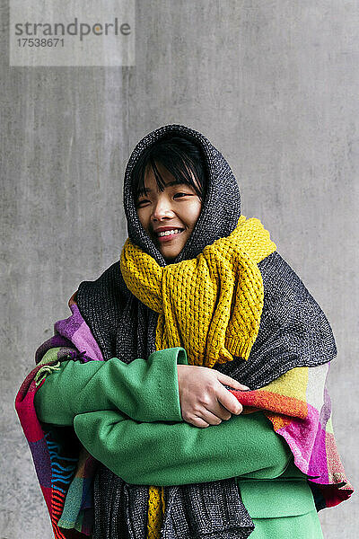 Smiling woman wearing warm clothing wrapped in blanket