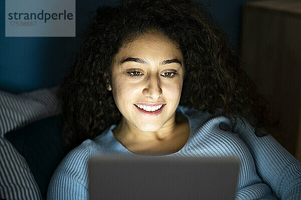 Lächelnde junge Frau benutzt Tablet-PC im Schlafzimmer