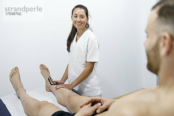 Smiling physical therapist looking at sportsman on massage table