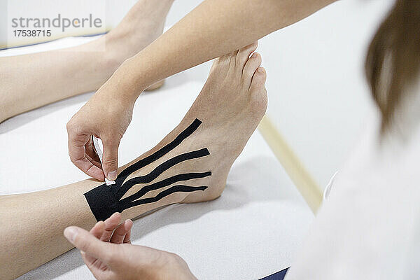 Physical therapist applying therapeutic tape on athlete's leg at massage table