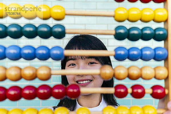 Smiling young woman looking through multi colored abacus