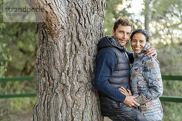 Mann lehnt an Baum und umarmt Frau im Park